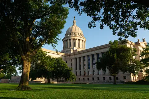 Oklahoma State Capitol dome and facade framed by trees on the Capitol lawn.